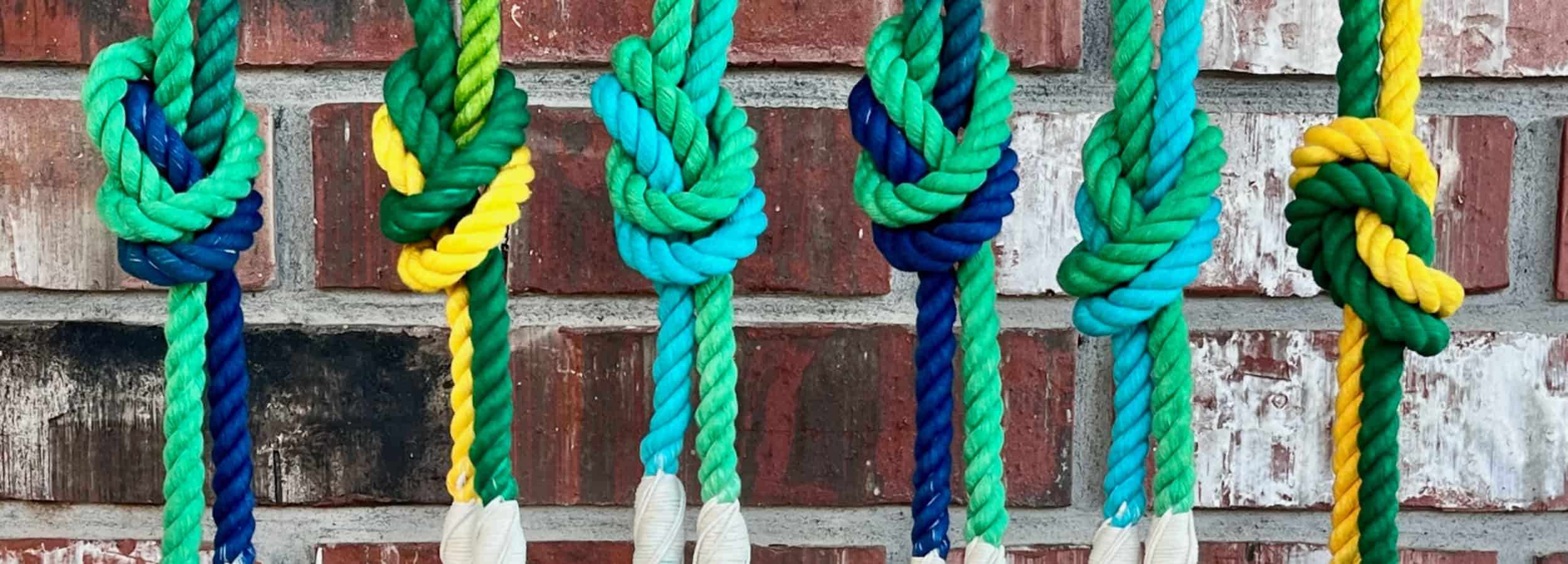 Colorful rope dog leashes with large knots tied in the middle against a brick wall background