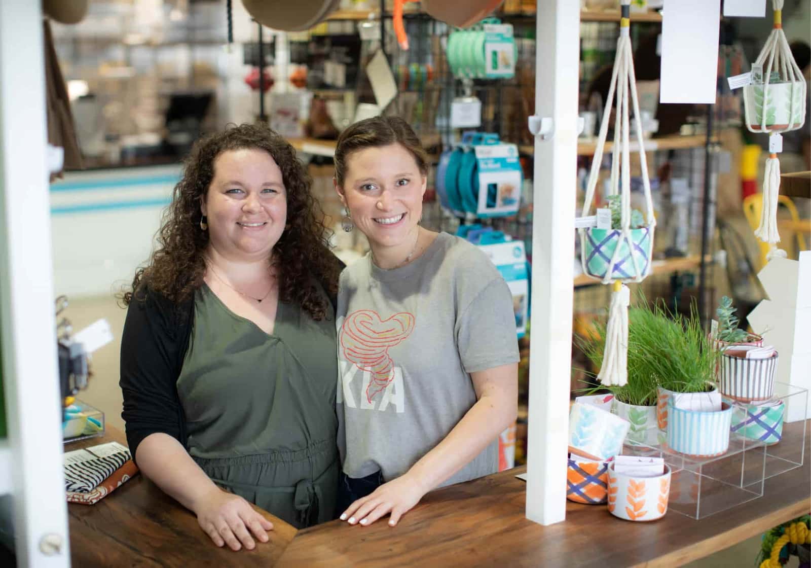 Two women smiling behind the counter at Knot Yours pet boutique in Tulsa, surrounded by colorful pet gear and handmade goods.