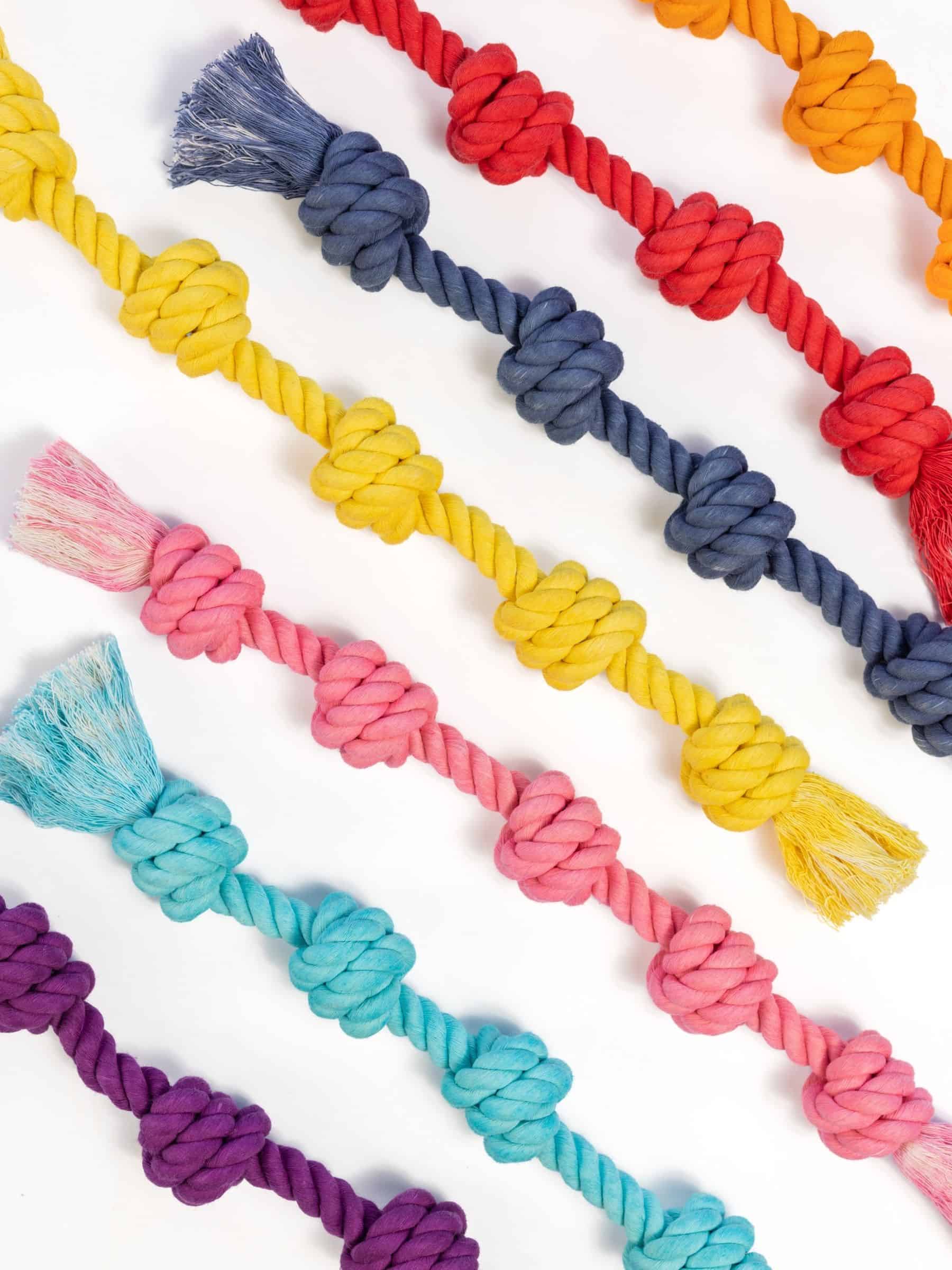 Flat lay of Little Gigantic dog rope toys arranged diagonally in colors including orange, red, navy, yellow, pink, aqua, and purple. This image showcases the full range of indestructible rope toys for small dogs.