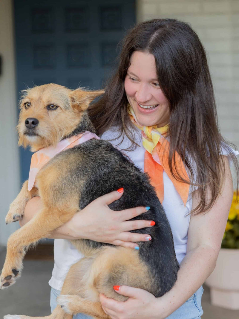 Woman holding a dog with both wearing a matching handmade orange and yellow bandana