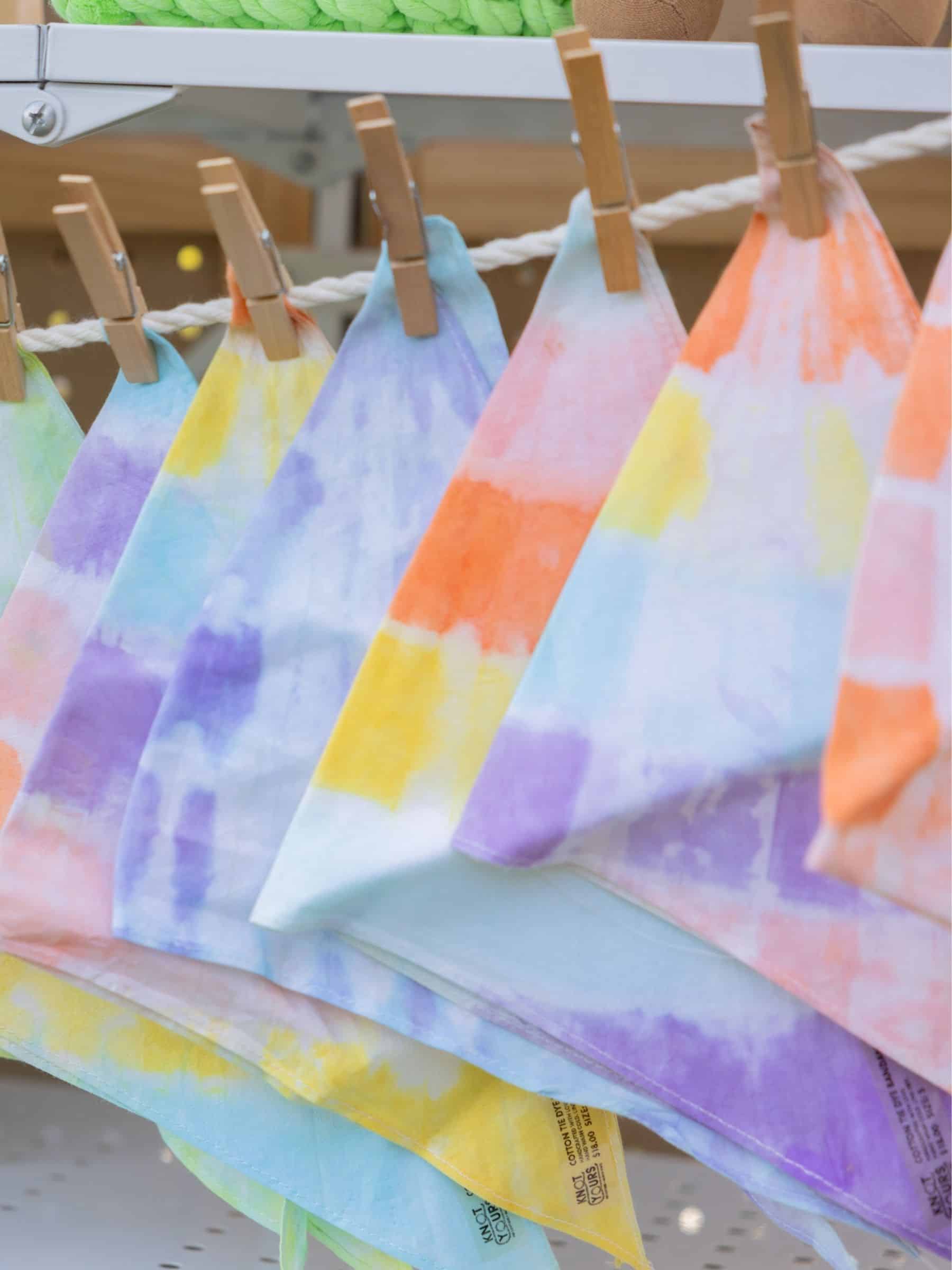 Colorful hand-dyed dog bandanas hanging on a rack with wooden clips.