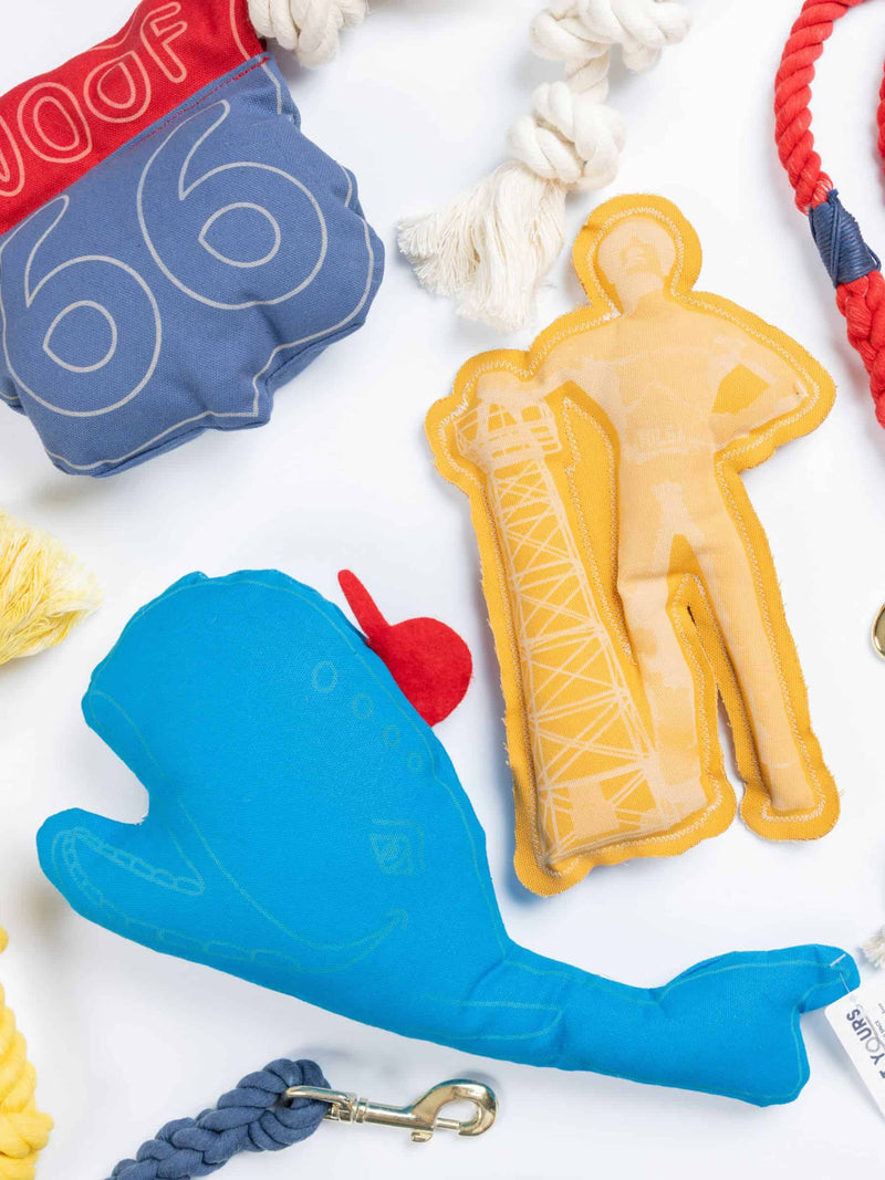 Flatlay of handmade blue whale squeaky dog toy surrounded by other rope and canvas toys