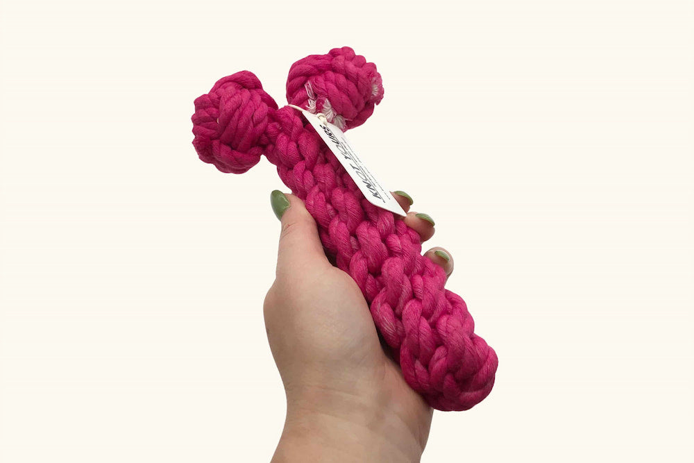 A hand holds a vibrant hot pink rope bone dog toy with a Knot Yours tag, showing product size.