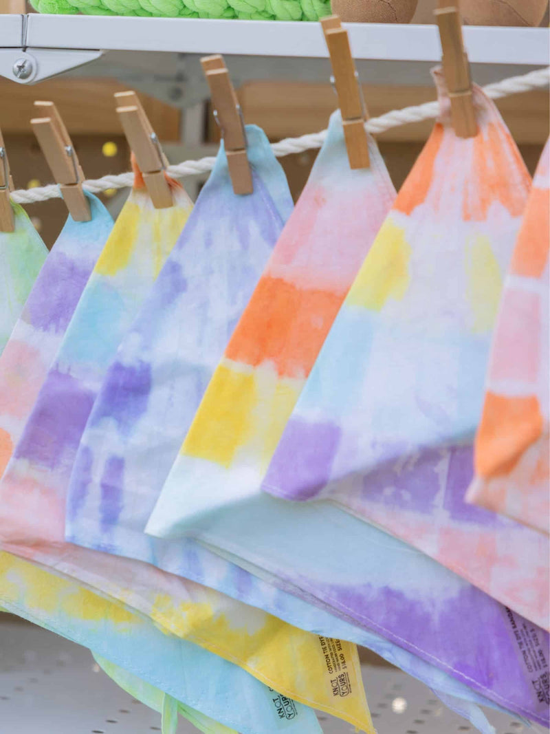 Colorful hand-dyed dog bandanas hanging on a rack with wooden clips.